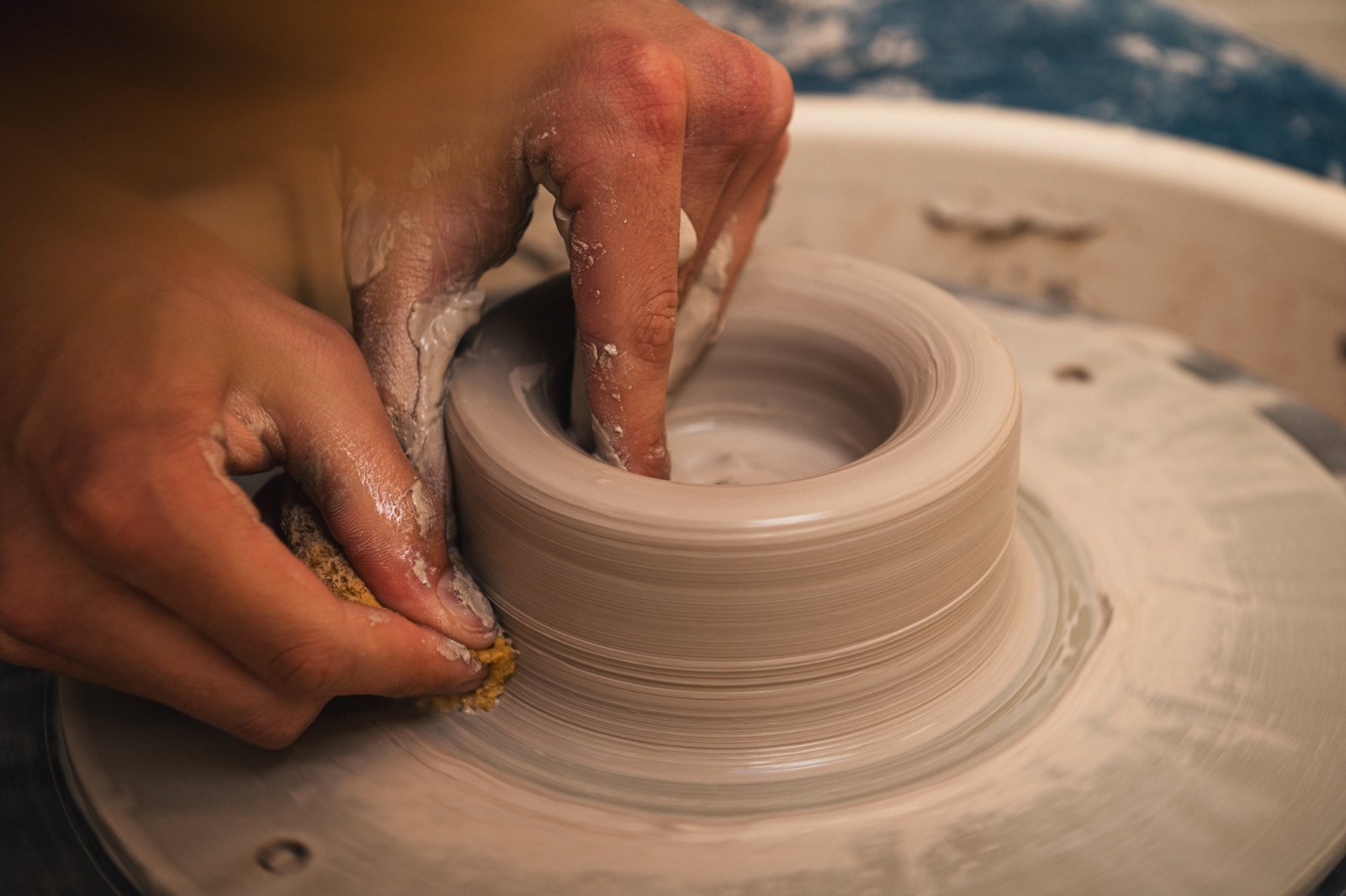 Hands shaping the inside of a clay form on the wheel